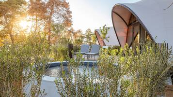 Un área lounge al aire libre y moderna con piscina, rodeada de árboles y una estructura única tipo tienda.