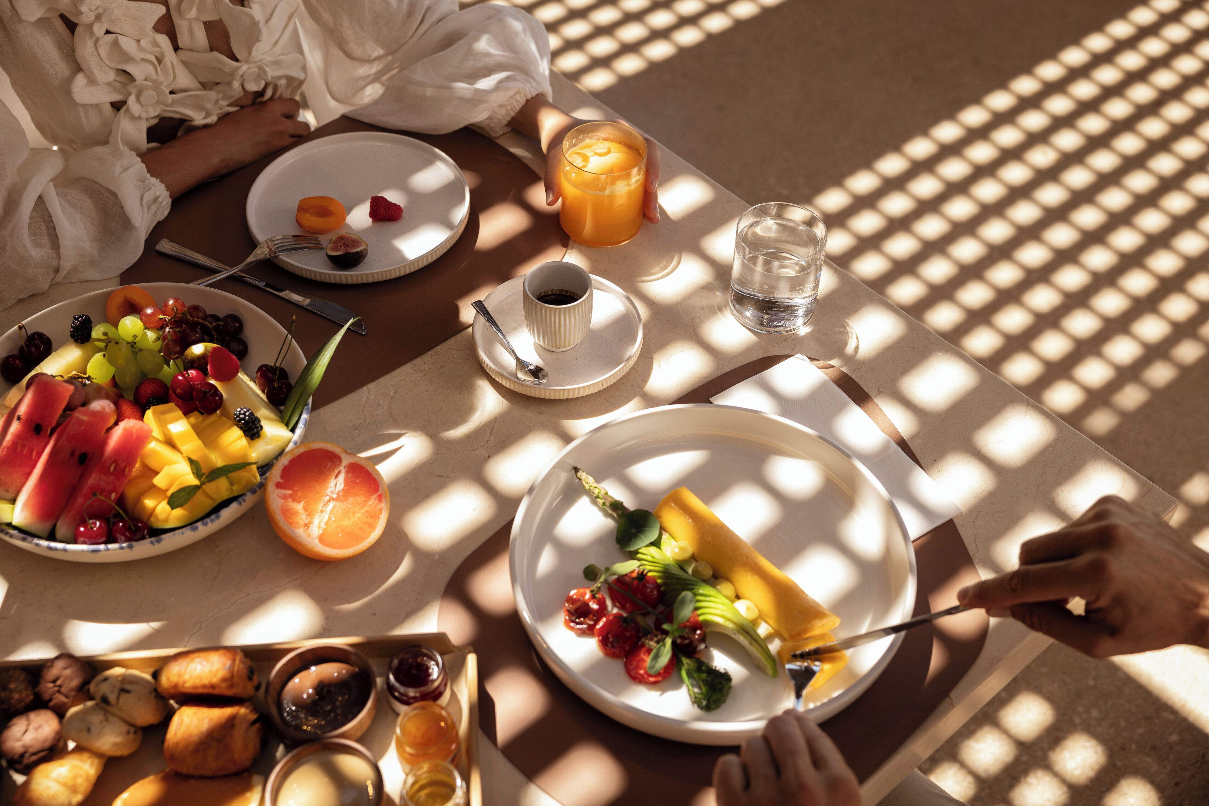 A breakfast setting with plates of fruit, a glass of orange juice, and a cup of coffee.