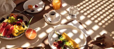 A breakfast setting with plates of fruit, a glass of orange juice, and a cup of coffee.