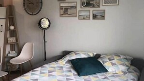 A bedroom with a bed, a chair, a desk, and a wall clock. - Logement 1 à 6 P- 150m Plage- Jardin et Parking (Courseulles-sur-Mer)