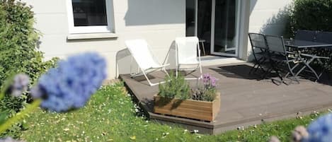 A modern patio with a wooden deck, white lounge chairs, and a table with chairs.