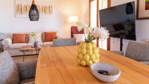 Un salon avec une table en bois, un vase de fleurs, un canapé et un téléviseur.