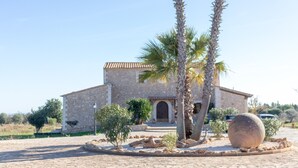 Un bâtiment en pierre surmonté d’un toit de tuiles, entouré de palmiers et avec une grande sphère de pierre en premier plan.