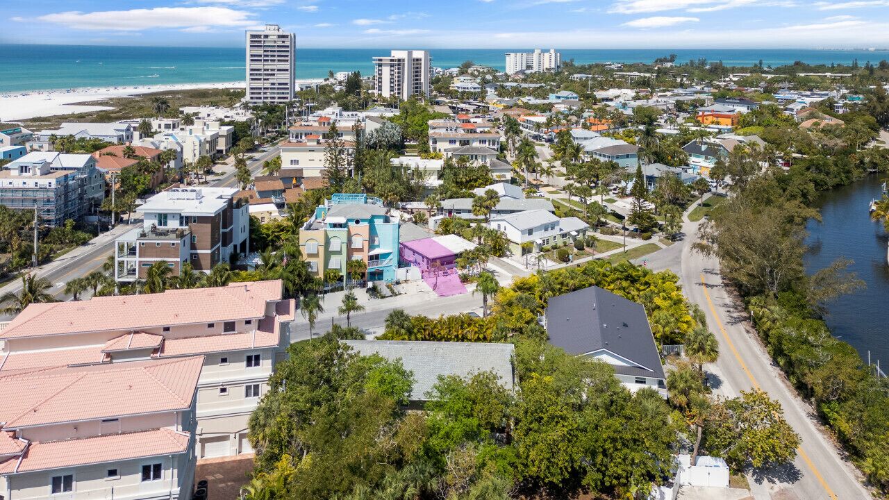 An aerial view of a coastal residential area with buildings, a beach, and a river.