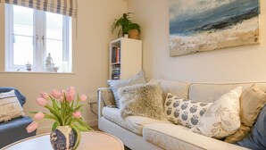 Un salon avec un canapé, une table ornée d’un vase de fleurs, une bibliothèque et un tableau accroché au mur.
