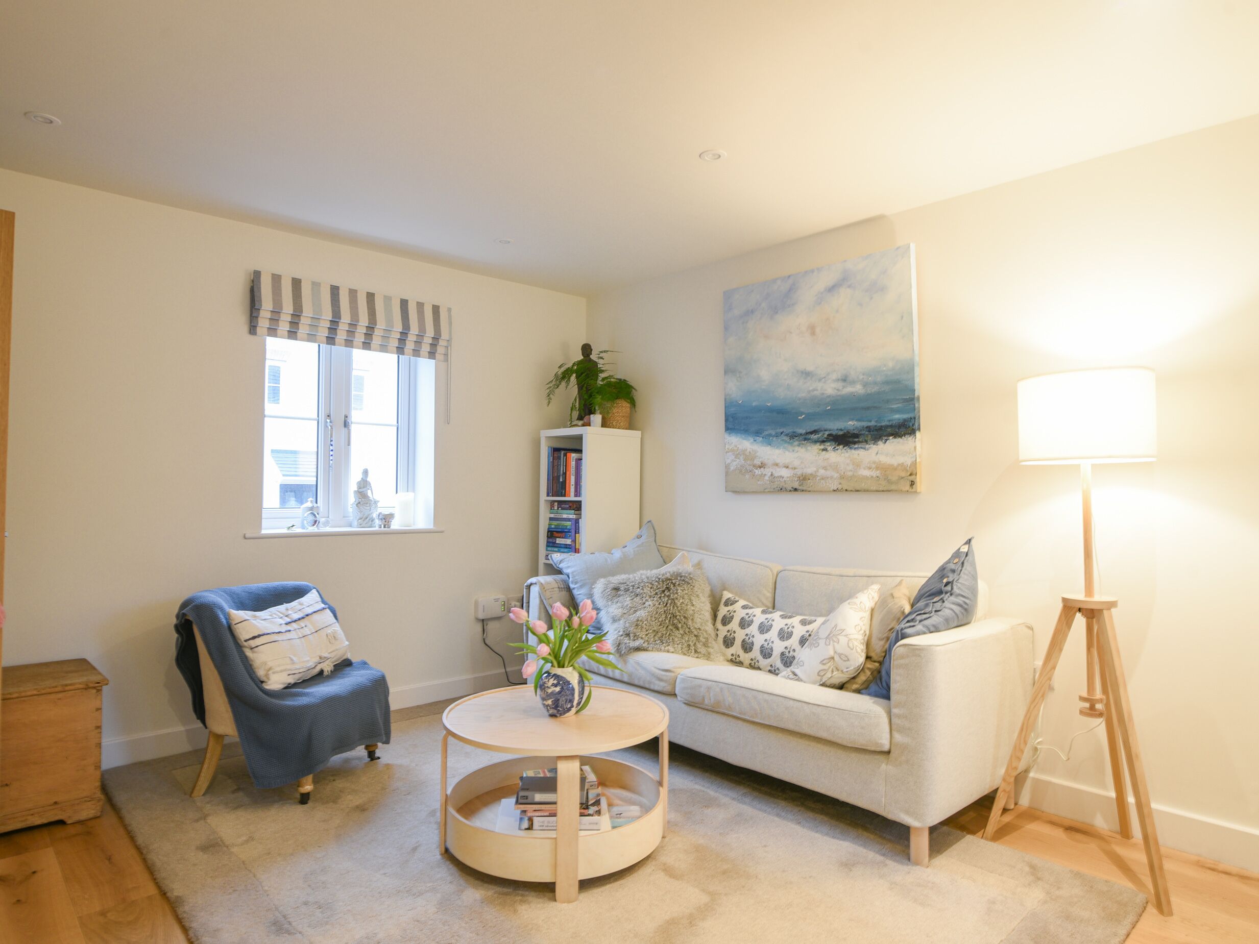 A living room with a sofa, armchair, round coffee table, bookshelf, and a painting on the wall.