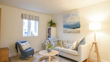 A living room with a sofa, armchair, round coffee table, bookshelf, and a painting on the wall.