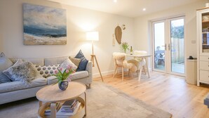 Un salon avec un canapé, une table basse, une lampe et un tableau représentant une scène de plage.