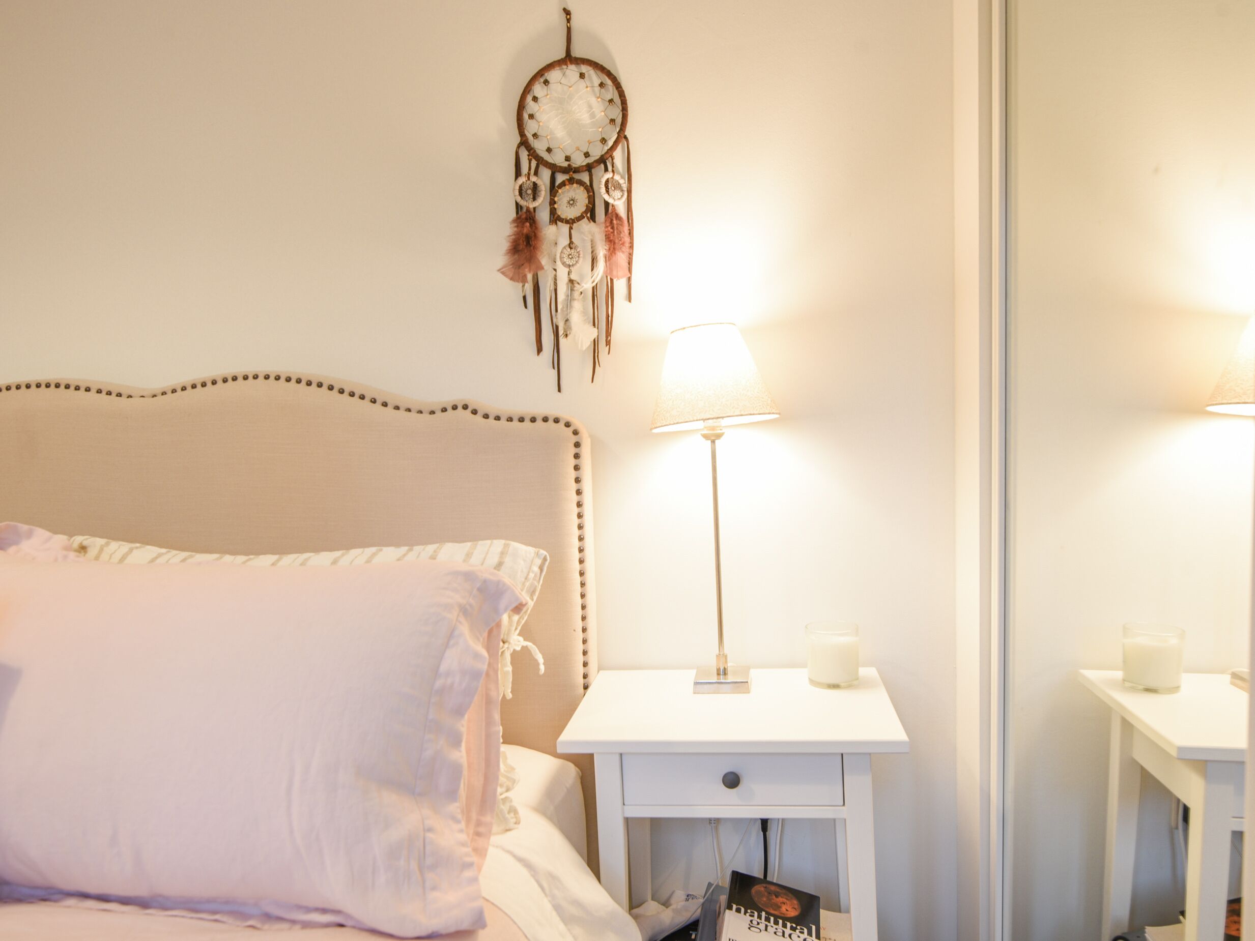 A bedroom with a bed, a nightstand with a lamp, and a dreamcatcher on the wall.