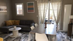 Una sala de estar con un sofá gris, una mesa redonda, una mesa de comedor con sillas y un piso estampado.