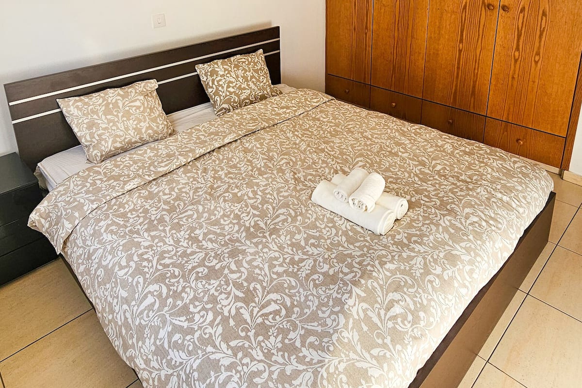 A bedroom with a large bed, wooden wardrobe, and a nightstand.