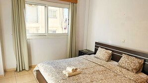 A bedroom with a bed, a nightstand, a window with curtains, and a ceiling light. - Unique City Rooms (Larnaca)