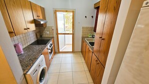 A compact kitchen with wooden cabinets, a washing machine, and a sink. - Unique City Rooms (Larnaca)