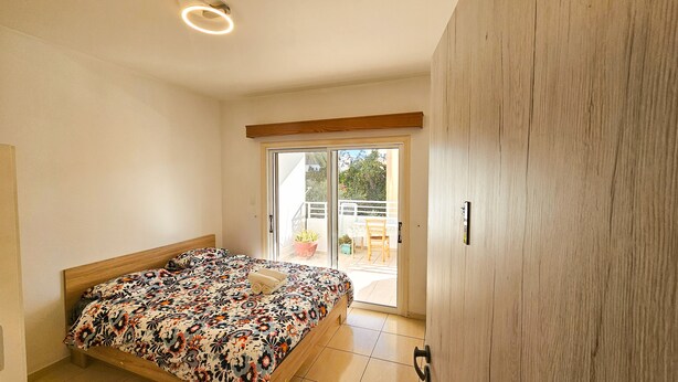 A bedroom with a bed, a sliding glass door to a balcony, and a wooden wardrobe. - Unique City Rooms (Larnaca)