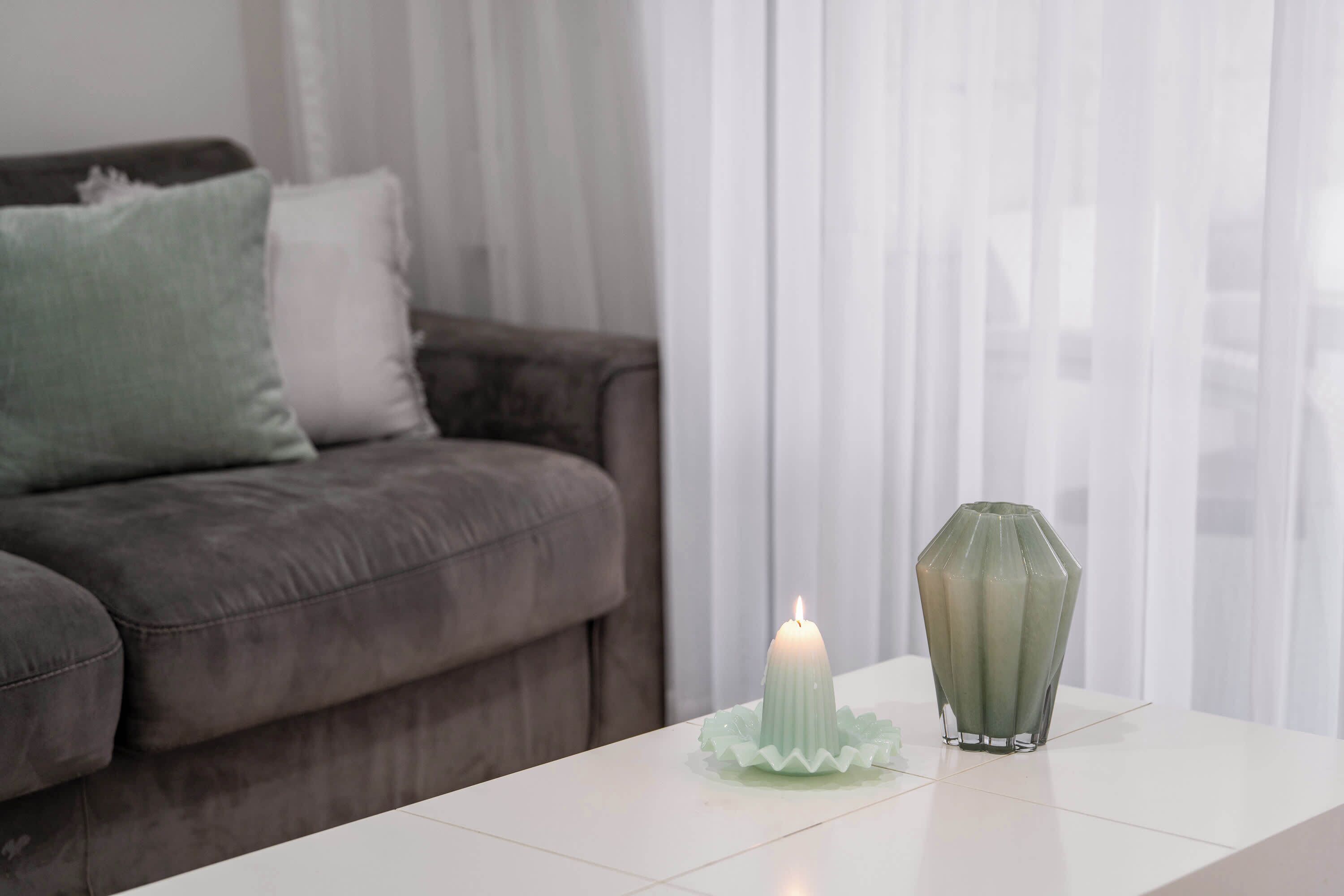 Un salón con una mesa blanca, un florero verde y una vela encendida.