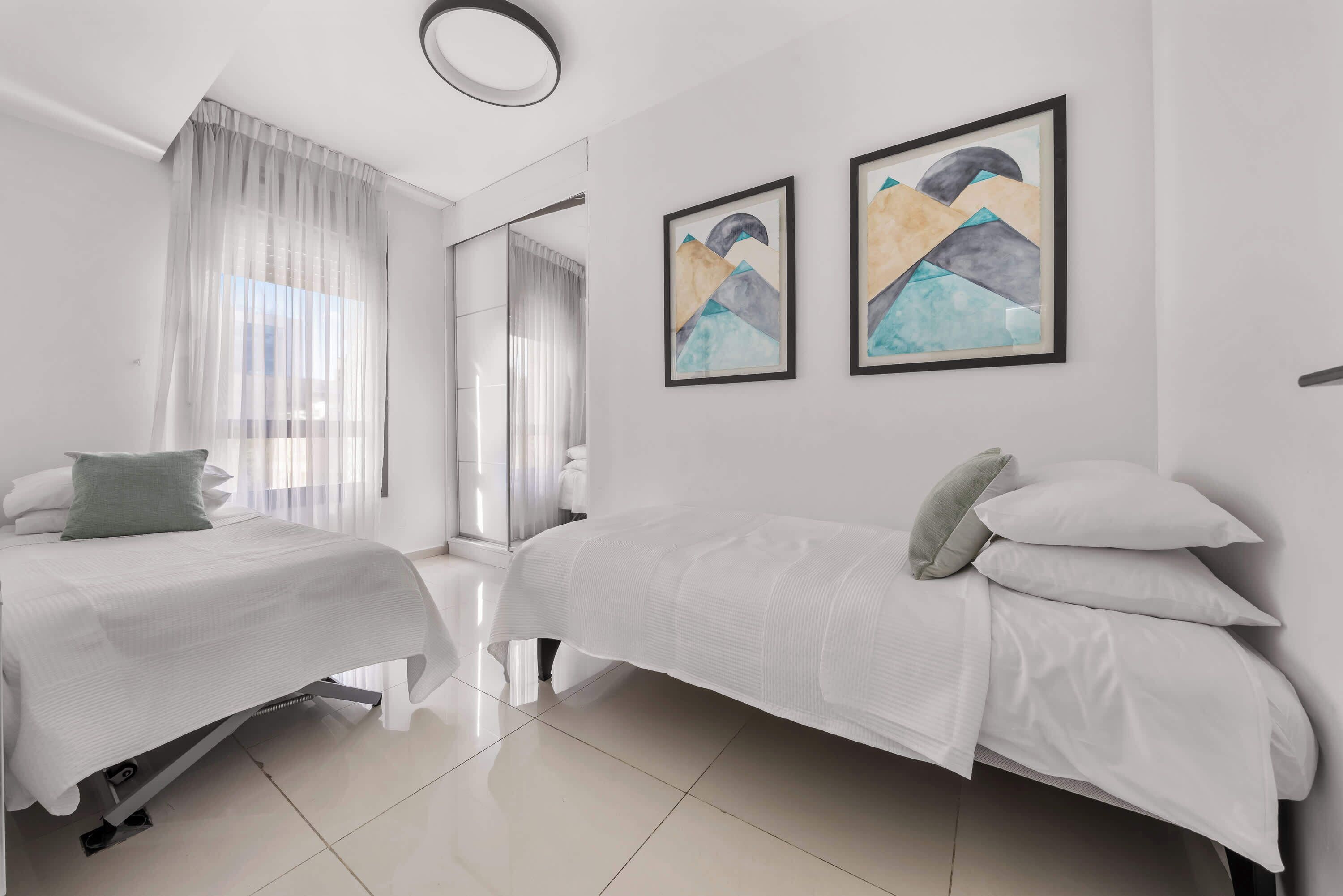 Une chambre d’hôtel moderne avec deux lits, un grand miroir et des œuvres d’art abstraites accrochées au mur.