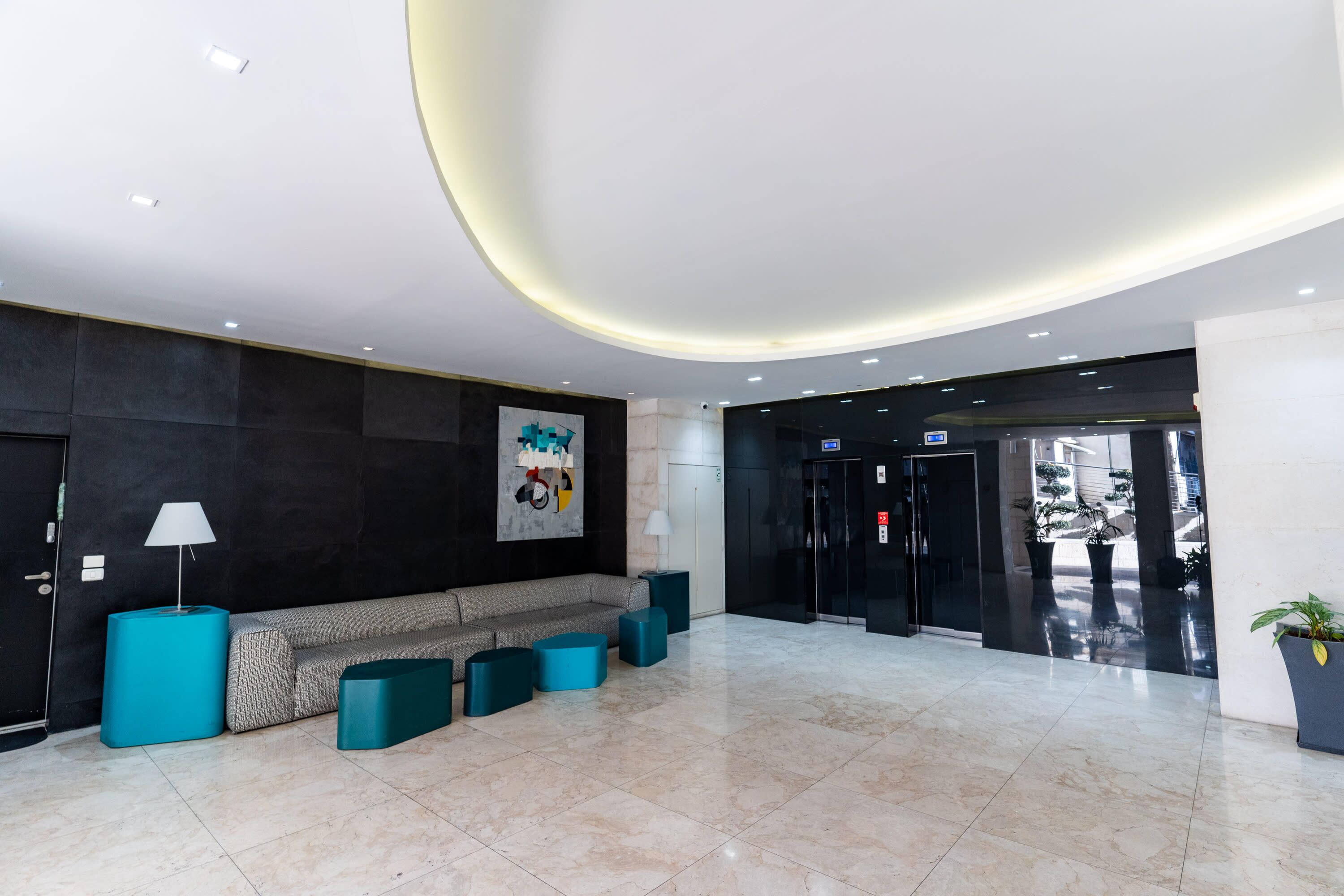 A modern lobby with a sofa, teal ottomans, a lamp, and a painting on the wall.
