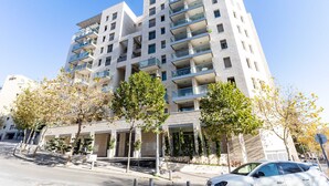 Un edificio residencial de varios pisos con balcones, entrada porticada y zona de estacionamiento.