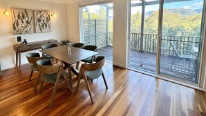 A spacious room with a wooden dining table and chairs, a large sliding glass door leading to an outdoor deck with a view of trees and hills.