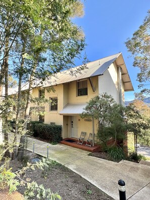 A two-story building with a flat roof, a front porch with two chairs, and a small garden area.