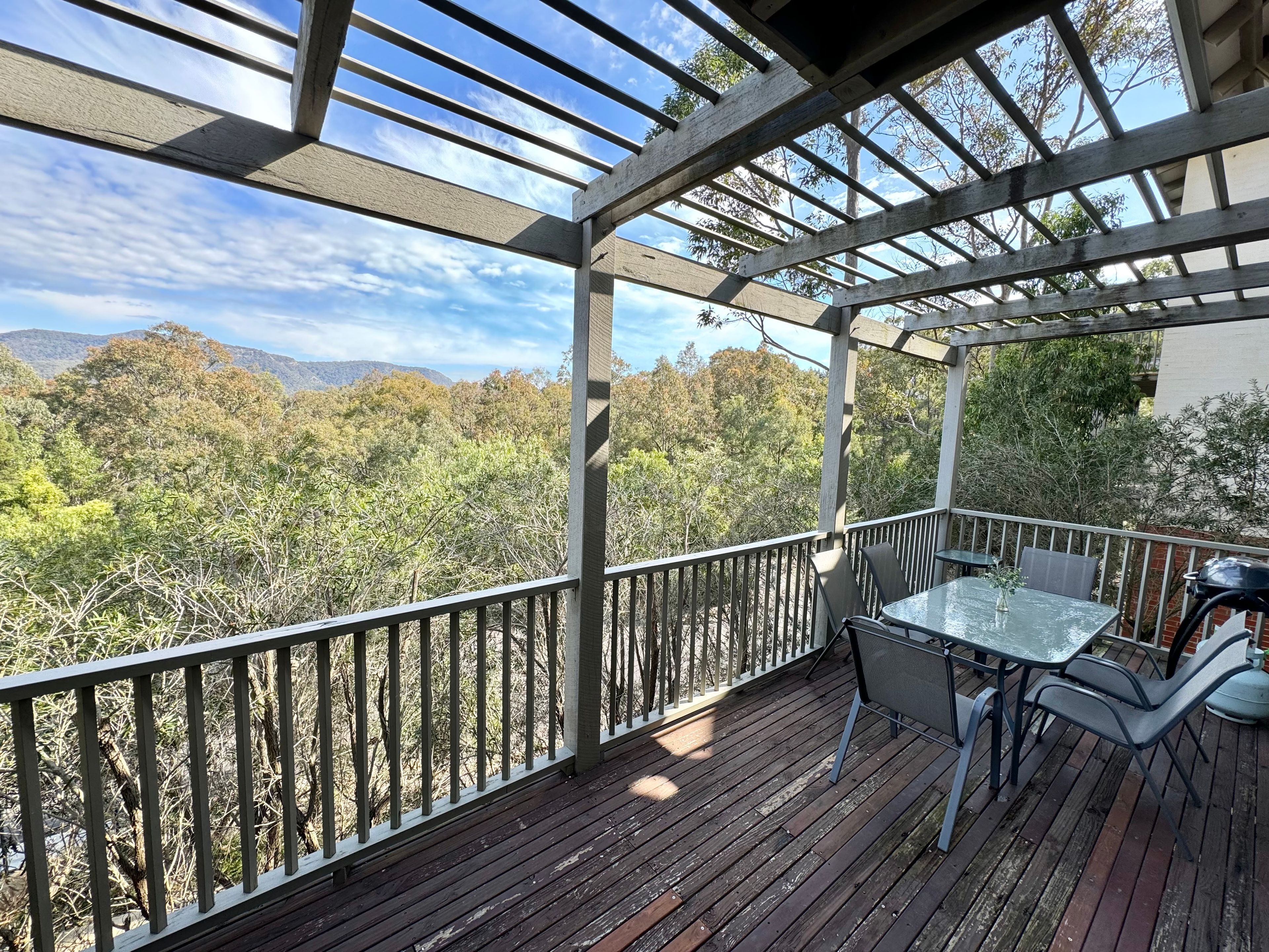 Eine Holzterrasse mit Tisch und Stühlen, die auf eine bewaldete Landschaft mit Bergen im Hintergrund blickt.