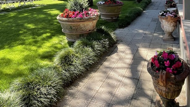A pathway lined with large flower pots, leading to a lush green lawn and a mountainous backdrop.