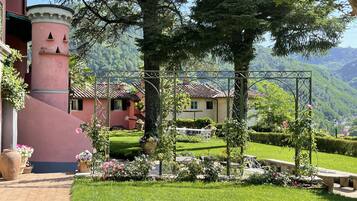 A garden with a gazebo, a pink building, and a view of a mountain.
