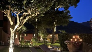 A nighttime outdoor area with lounge chairs, a well-lit garden, and a building in the background.