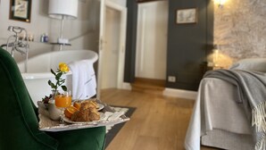 A cozy room with a wooden ceiling, a bathtub, a dining table with breakfast, and a bed.
