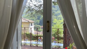 A window with white curtains, a view of a balcony with a metal railing, and a tree in the background.