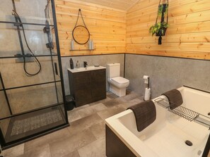 A modern bathroom with a glass shower enclosure, a wooden vanity, a toilet, and a bathtub with a towel. - Height End Farm Log Cabin (Bacup)