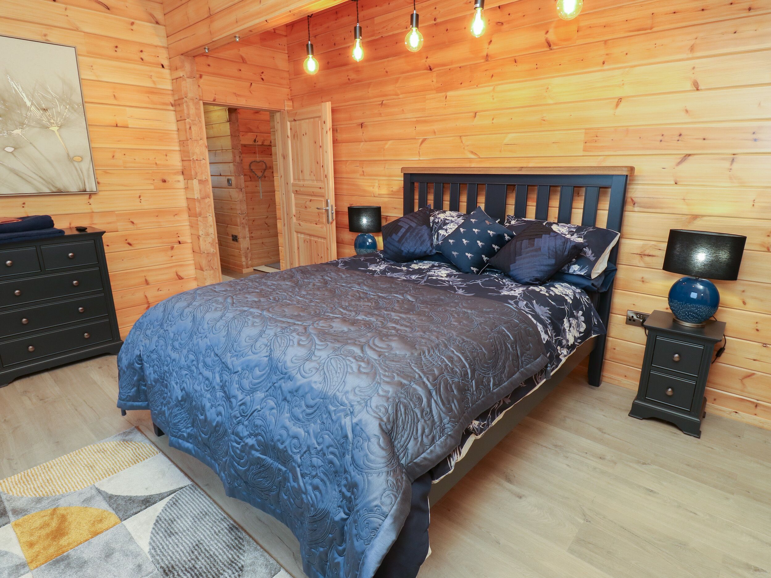 Un dormitorio con paneles de madera, una cama, mesitas de noche y una lámpara fijada a la pared.
