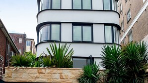 A modern multi-story building with a curved facade, large windows, and a stone retaining wall with plants. - Kirribilli Charisma I90 (Kirribilli)