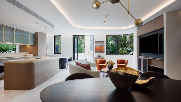 A modern kitchen with a central island, a dining area with a round table and chairs, and a living space with a flat-screen TV and seating. - Kirribilli Charisma I90 (Kirribilli)