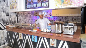 A bar area with a TV screen displaying 'Frobeat Mix 2024', a coffee machine, and various bar supplies. - Fuego Hotel (Kampala)