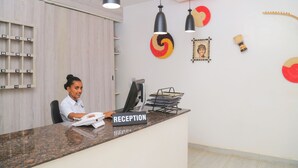 A reception desk with a 'RECEPTION' sign, a telephone, and a computer. There are wall-mounted shelves with numbered compartments, a red and yellow wall decoration, and a framed picture. - Fuego Hotel (Kampala)