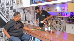 A bar area with a patterned wall, a counter with a bottle of liquor, and a TV screen displaying "AFROBEAT MIX 2024". - Fuego Hotel (Kampala)