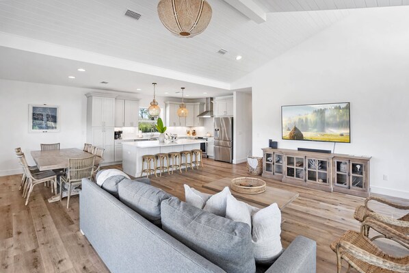 A modern kitchen with white cabinets, a central island with stools, and a large flat-screen TV mounted on the wall.