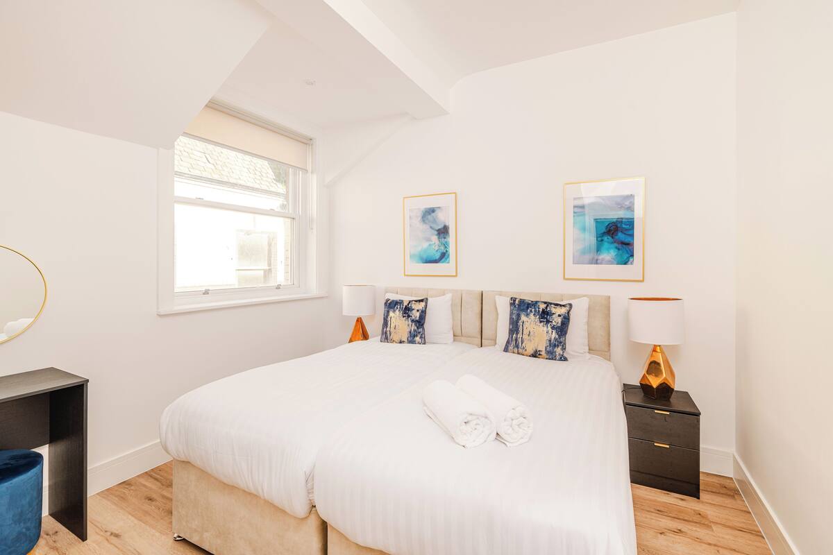 Un dormitorio moderno con una cama grande, dos mesitas de noche, un ventanal y una obra de arte en la pared.