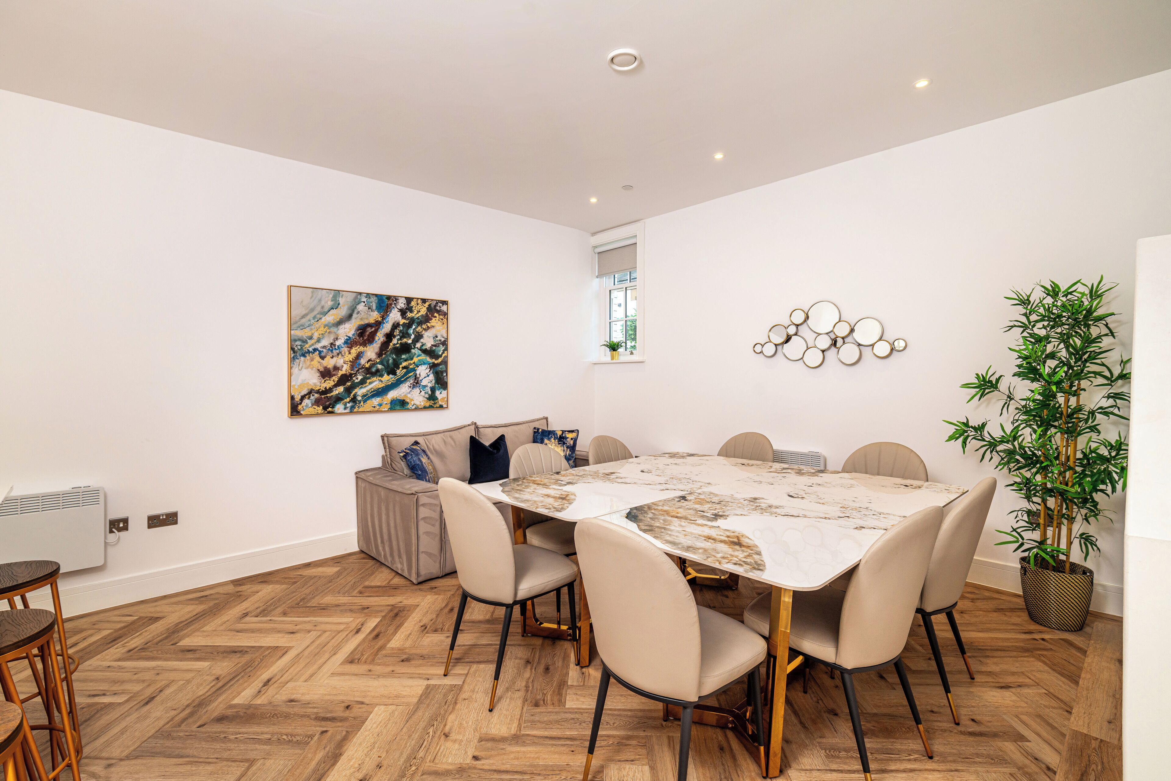 A dining area with a marble table, six chairs, a sofa, a potted plant, and a wall art piece.