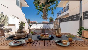 A wooden table set with plates of food, a pineapple centerpiece, and drinks, with a view of a building and a clear sky.