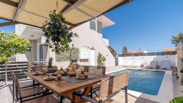 A poolside dining area with a table, chairs, and a hanging plant.