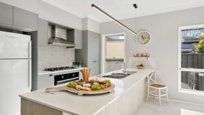 A modern kitchen with a central island, white cabinetry, a built-in oven, and a large window providing natural light.