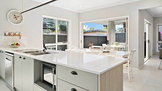 A modern kitchen with a central island, built-in appliances, and large windows offering views of the backyard.