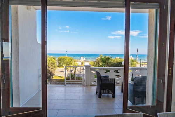 A balcony with a view of the sea, a white railing, and two black chairs.