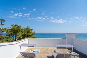 Une terrasse sur le toit avec deux chaises longues, une table et une vue sur la mer.