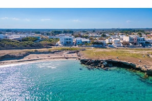 A coastal town with clear turquoise waters, a rocky beach, and modern buildings.