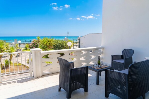 A balcony with wicker furniture, a table with a bottle, and a view of the ocean.