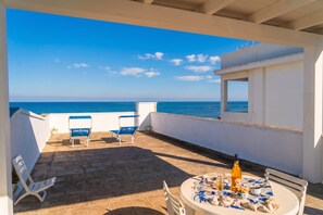 Une terrasse avec une table dressée pour le repas, une chaise et une vue sur la mer.