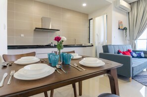 Une table à manger dressée avec des assiettes, des couverts et des tasses bleues, un vase rempli de fleurs et un canapé gris dans un salon moderne.